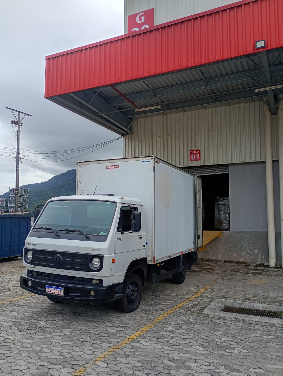 O caminhão baú do Lima encostado na doca de um galpão para carregar